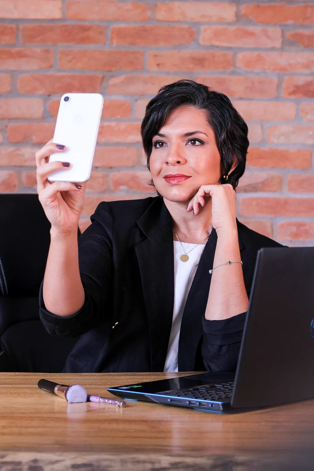 Empresária sorrindo com o celular na mão, ao lado do notebook