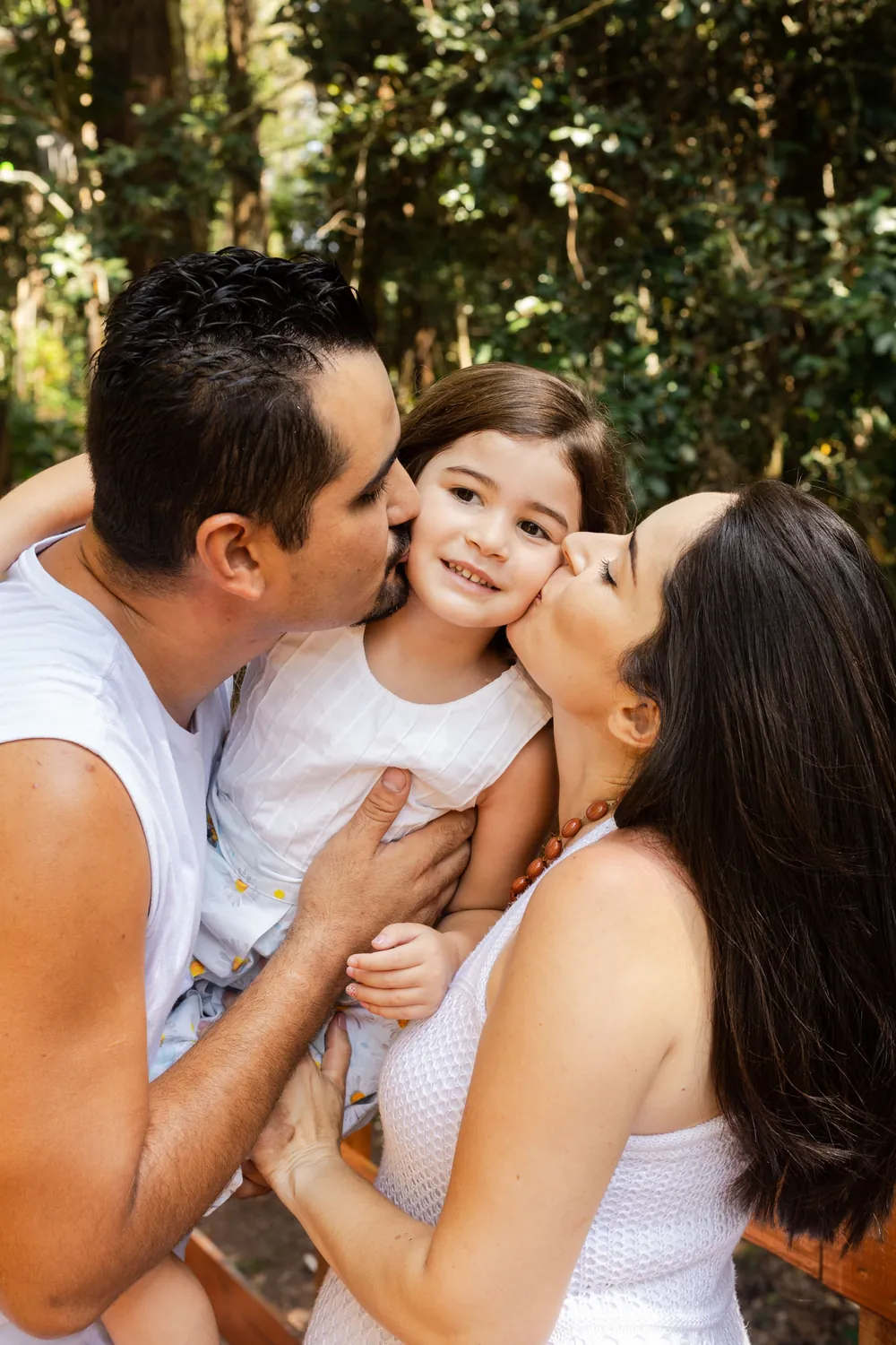Pai e mãe dão um beijo na filha pequena